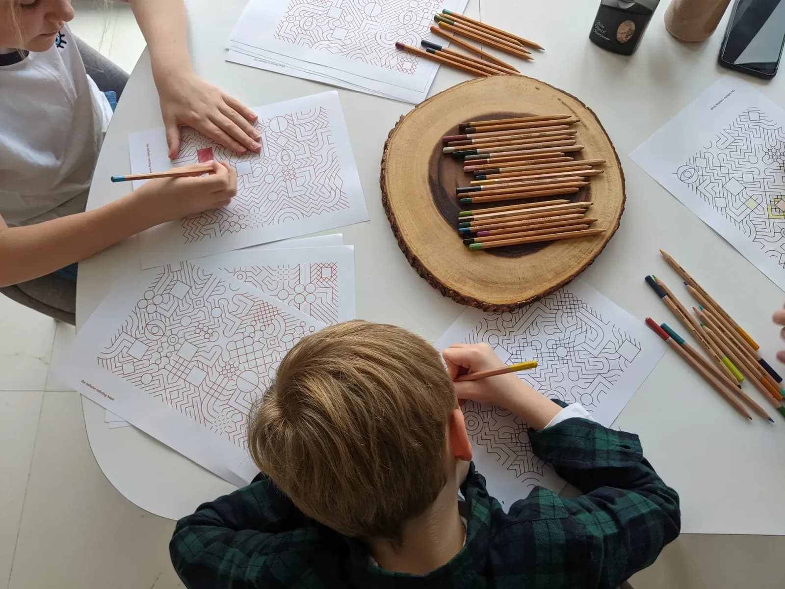 A close photograph of hands and colouring pencils beside a partly coloured printed pattern